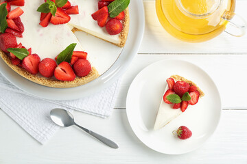 Delicious cheesecake with strawberries, mint and tea on white wooden table, flat lay