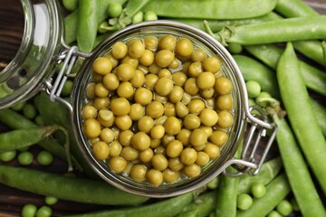 Pickled peas in jar and pods on wooden table, flat lay