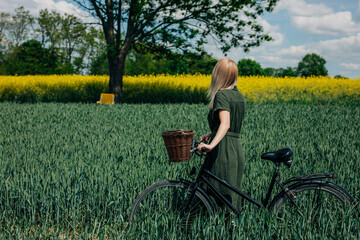 Woman with vintage bicycle in a rural field with green wheat and yellow rapeseed
