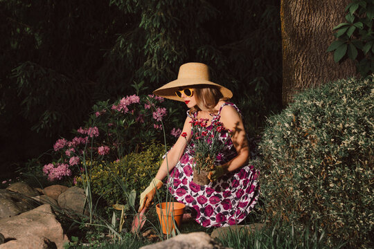 Stylish woman in retro dress gardening with flowers in spring sunlight