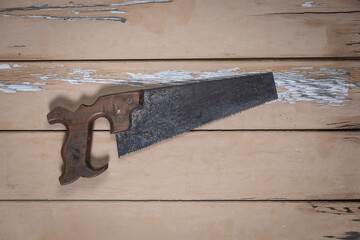 Old handsaw placed in the center on a rustic beige wooden table.
