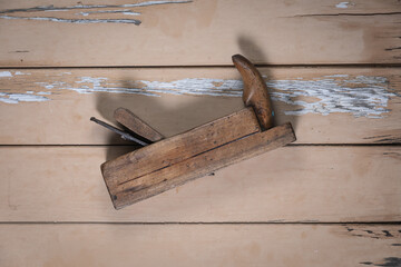 Old wooden hand plane placed diagonally in the center on a rustic beige wooden table.
