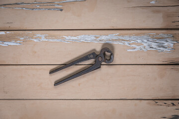Old pincers placed in the center on a rustic beige wooden table.

