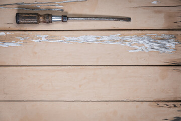 Large flathead screwdriver with wooden handle placed at the top left corner on a rustic beige...