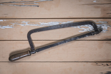 Old bow saw placed diagonally in the center on a rustic beige wooden table.
