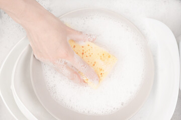 Female hand with sponge for washing dishes and bowls in water with foam or dishwashing liquid. washing dishes in the sink