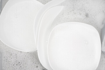 clean white dishes in soapy foam for washing