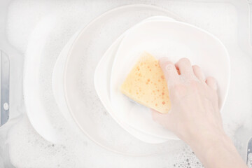 Female hand with sponge for washing dishes and bowls in water with foam or dishwashing liquid. washing dishes in the sink