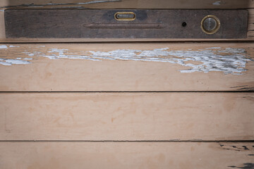 Ancient wooden spirit level placed at the top edge of a rustic beige wooden table. Space is left...