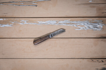 Folding knife with wooden handle and sheepfoot blade placed in the center on a rustic beige wooden...