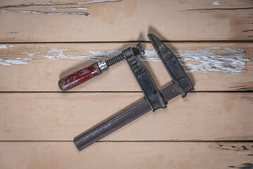 Old metal clamp with wooden handle placed diagonally in the center on a rustic beige wooden table.
