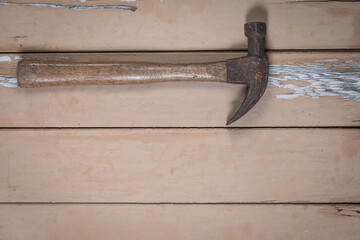 Old hammer with wooden handle placed at the top left corner on a rustic beige wooden table. Space...
