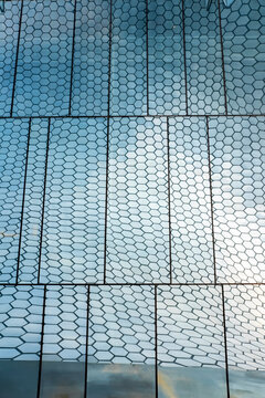Modern glass facade featuring hexagonal patterns and subtle reflections of sky, creating a geometric contemporary urban surface with light textures and rhythmic architectural design.
