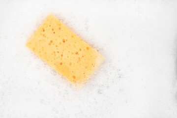 White pure foam with sponge for washing dishes. dishwashing foam and yellow sponge close up