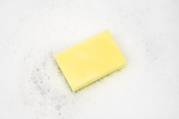 White pure foam with sponge for washing dishes. dishwashing foam and yellow sponge close up