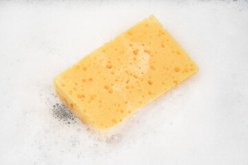 White pure foam with sponge for washing dishes. dishwashing foam and yellow sponge close up