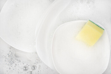 Yellow sponge for washing with dishes and bowls in water and foam or dishwashing liquid. washing dishes in the sink