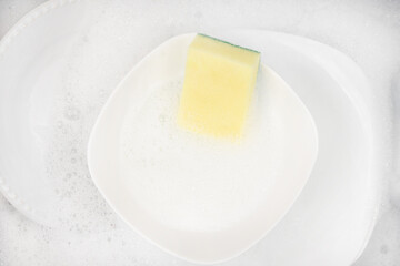 Yellow sponge for washing with dishes and bowls in water and foam or dishwashing liquid. washing dishes in the sink