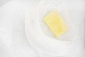 Yellow sponge for washing with dishes and bowls in water and foam or dishwashing liquid. washing dishes in the sink