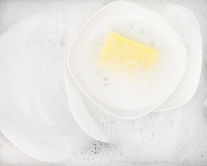 Yellow sponge for washing with dishes and bowls in water and foam or dishwashing liquid. washing dishes in the sink