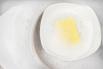 Yellow sponge for washing with dishes and bowls in water and foam or dishwashing liquid. washing dishes in the sink