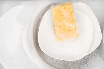 Yellow sponge for washing with dishes and bowls in water and foam or dishwashing liquid. washing dishes in the sink