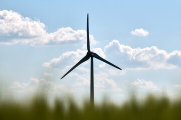 Single wind turbine silhouetted against bright blue sky with scattered fluffy clouds and blurred...
