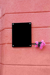 Black blank memorial plaque with pink carnation flower bouquet on coral color wall background.