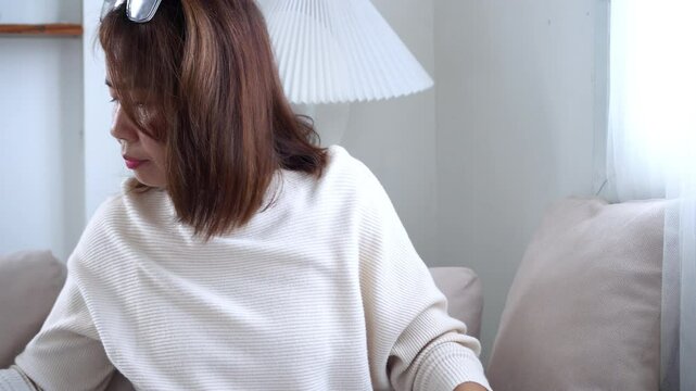 Asian woman looking for her glasses around the sofa area, then realizing they&rsquo;re on her head, showing forgetfulness that could be an early sign of memory problems or Alzheimer 