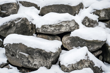 Snow-covered large rocks stacked irregularly, with white snow contrasting against dark gray stones in a natural outdoor setting.