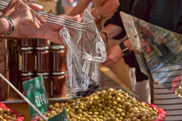 Hands of a vendor filling a bag with black olives at a typical Provenzal market in Aix-en-Provence
