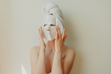 Young woman relaxing at home with a hydrating facial sheet mask.  kincare routine, beauty...
