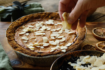 Sprinkle pumpkin pie with sliced almonds. Cooking homemade traditional Thanksgiving pie