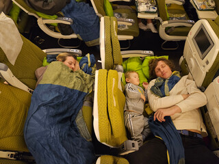 Man and a child are sleeping on a plane. A woman is sleeping on the other side of the plane. father...