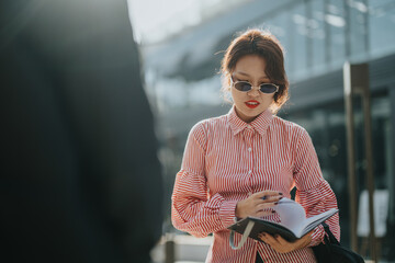 A fashionable woman in sunglasses reads a book outside on a sunny day, embodying confidence and...