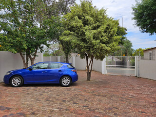 Blue car is parked in front of a white gate in courtyard house with pool in Johannesburg in South...