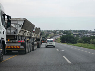 Truck with the letters on the back is driving down a road. A car is driving in front of the truck...