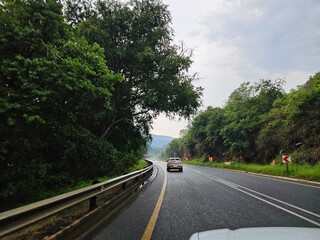 Car is driving down a road with a yellow line. The road is lined with trees. The car is on the right side of the road
