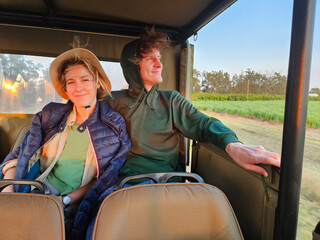 Man and a woman are sitting in a off-road car. The man is wearing a green hoodie during safari in...