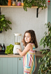Cute little girl making healthy drink green smoothie on home kitchen