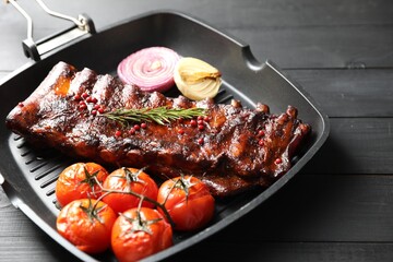 Delicious roasted pork ribs with rosemary, tomatoes and onions on grey wooden table, closeup