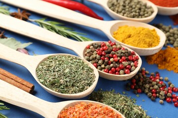 Different aromatic spices in spoons on blue background, closeup