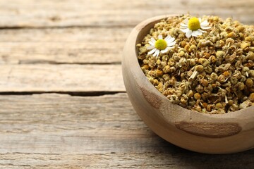 Dry and fresh chamomile flowers in bowl on wooden table, closeup. Space for text