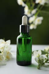 Essential oil and jasmine flowers on white table against blurred background, closeup