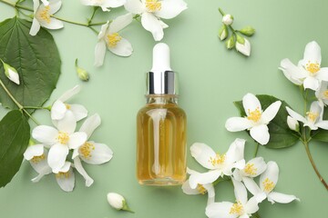 Essential oil and beautiful jasmine flowers on green background, flat lay