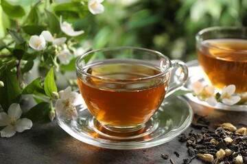 Aromatic jasmine tea in glass cups, brew and flowers on grey table outdoors, closeup