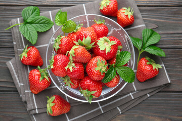 Fresh ripe strawberries and leaves in container on black wooden table, flat lay