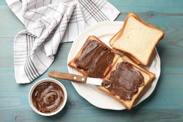 Tasty chocolate butter in bowl, slices of bread and knife on light blue wooden table, flat lay