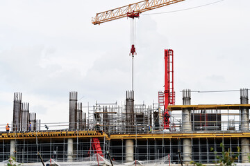 Highrise building under construction with tower crane, scaffolding, reinforced columns, steel framework, modern urban development in progress. Workers operate on top floor of concrete building site