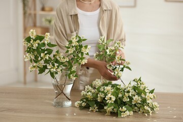 Woman making bouquet of jasmine branches at wooden table, closeup